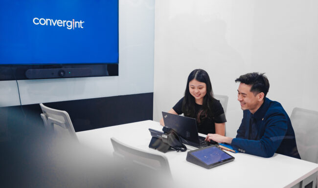 Two people working on laptop at office desk.