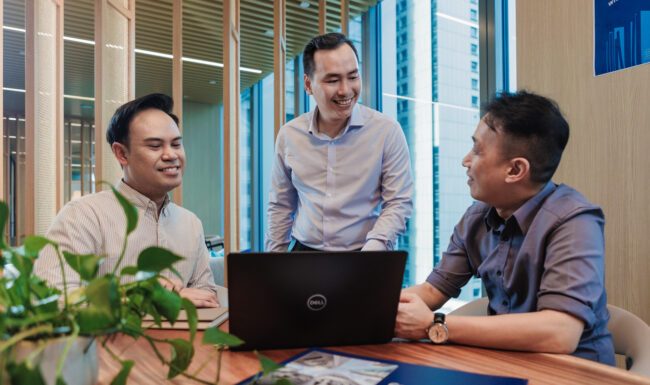 Three people working on laptops in office setting.