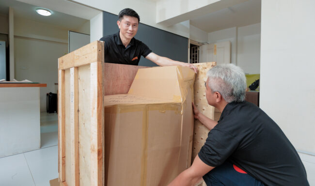 Two people moving a wooden shipping box.